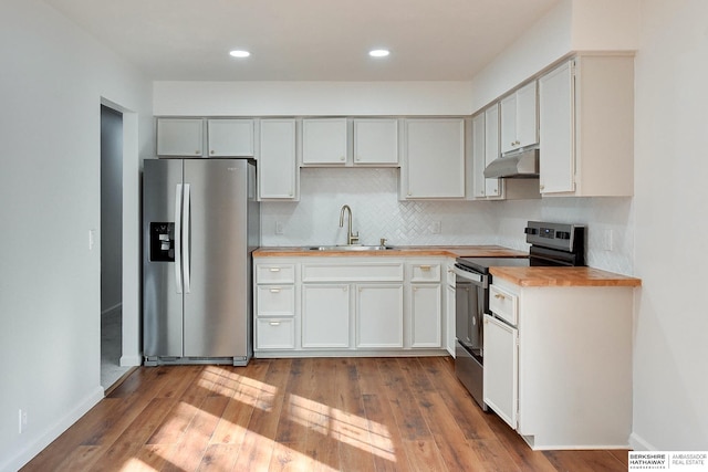 kitchen with a sink, stainless steel appliances, wood-type flooring, under cabinet range hood, and tasteful backsplash