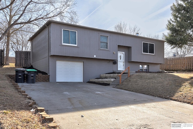 raised ranch featuring concrete driveway, an attached garage, and fence