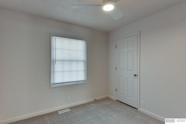 empty room featuring light carpet, visible vents, a ceiling fan, and baseboards