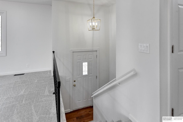 entrance foyer featuring baseboards, visible vents, dark colored carpet, and a chandelier