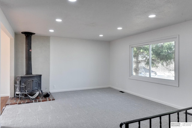 carpeted living room featuring recessed lighting, visible vents, baseboards, and a wood stove