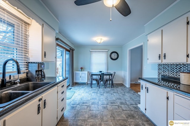 kitchen with a sink, decorative backsplash, crown molding, white cabinetry, and dark countertops