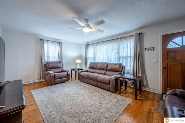 living area featuring visible vents, light wood-style flooring, a textured ceiling, and a ceiling fan