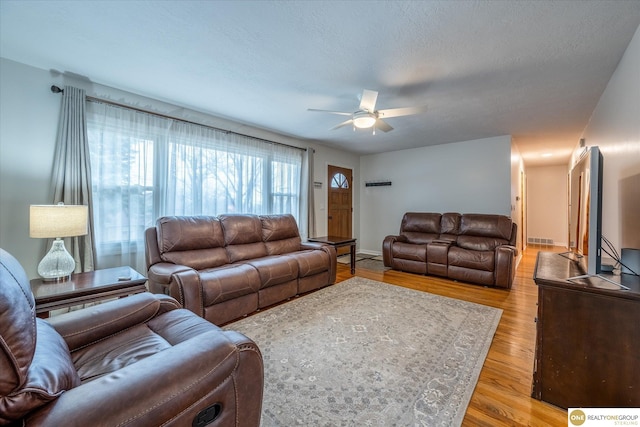 living area with visible vents, baseboards, light wood-type flooring, a textured ceiling, and a ceiling fan