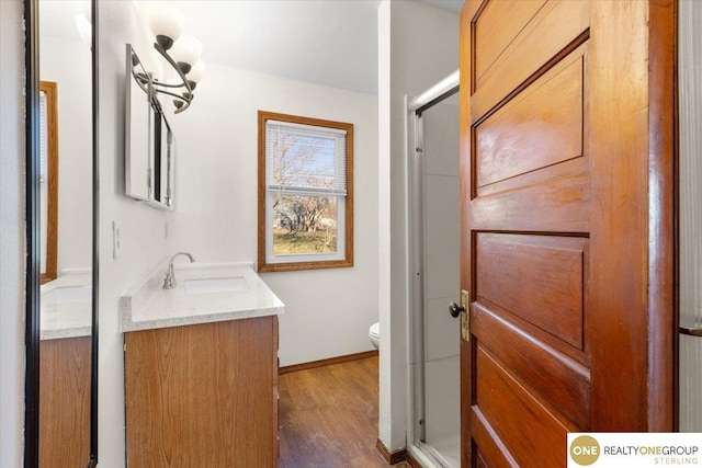bathroom featuring baseboards, toilet, wood finished floors, a shower with shower door, and vanity