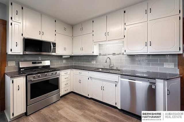 kitchen with a sink, backsplash, wood finished floors, white cabinetry, and appliances with stainless steel finishes