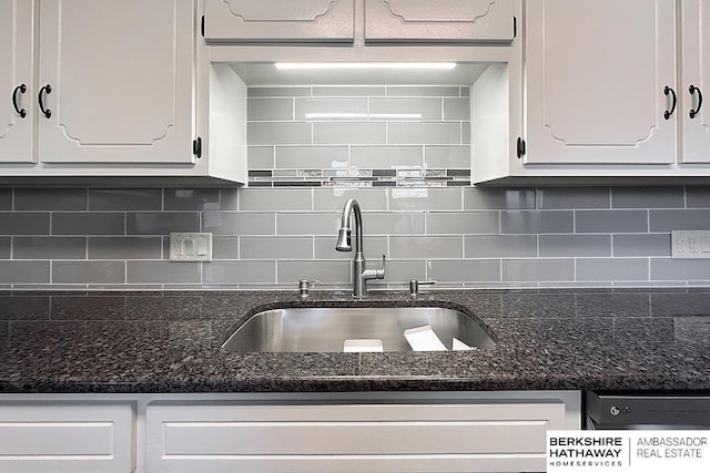 kitchen with white cabinetry, dark stone counters, backsplash, and a sink