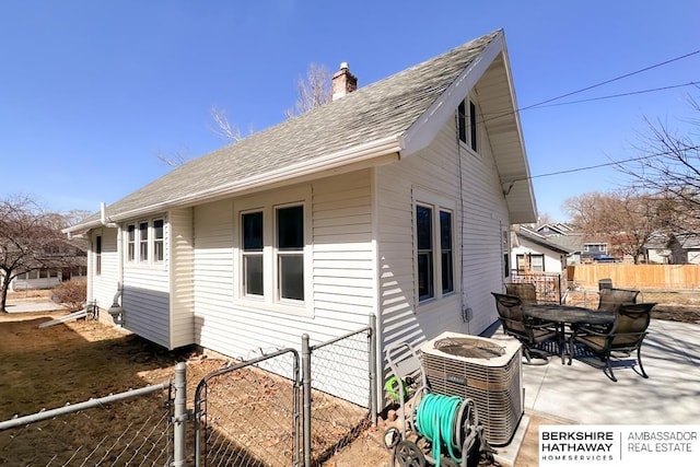 view of side of property featuring a shingled roof, fence, central AC, a chimney, and outdoor dining area