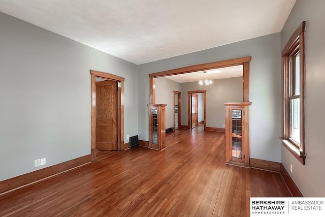 empty room with a notable chandelier, baseboards, and light wood finished floors