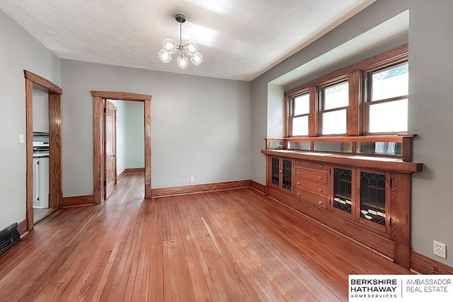 interior space with baseboards, a textured ceiling, a chandelier, and light wood finished floors