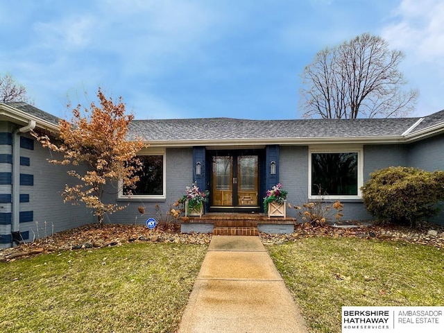 doorway to property with a lawn, brick siding, french doors, and a shingled roof