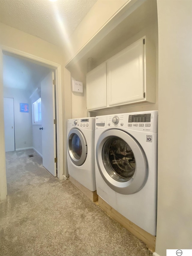 laundry area featuring washing machine and clothes dryer, light colored carpet, a textured ceiling, and cabinet space