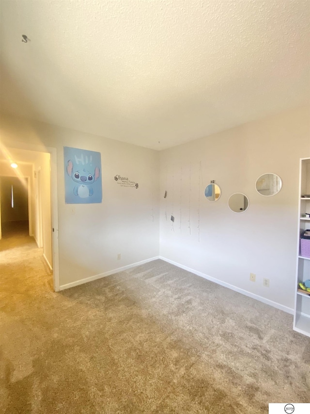 empty room with carpet, baseboards, and a textured ceiling