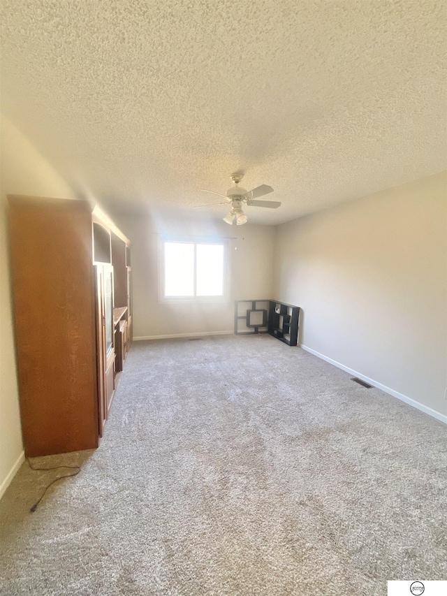 carpeted empty room featuring visible vents, a textured ceiling, baseboards, and ceiling fan