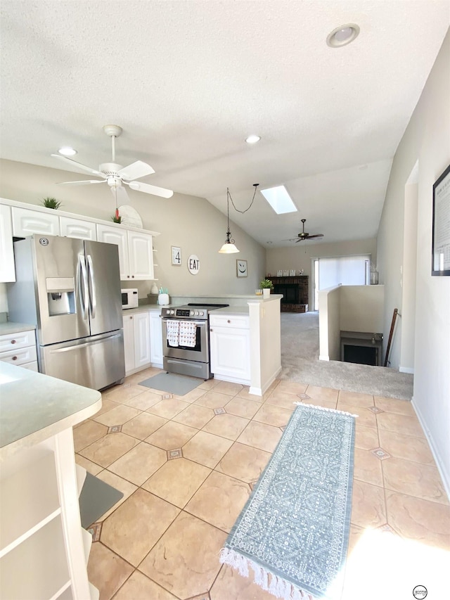 kitchen with lofted ceiling with skylight, appliances with stainless steel finishes, white cabinets, light countertops, and ceiling fan