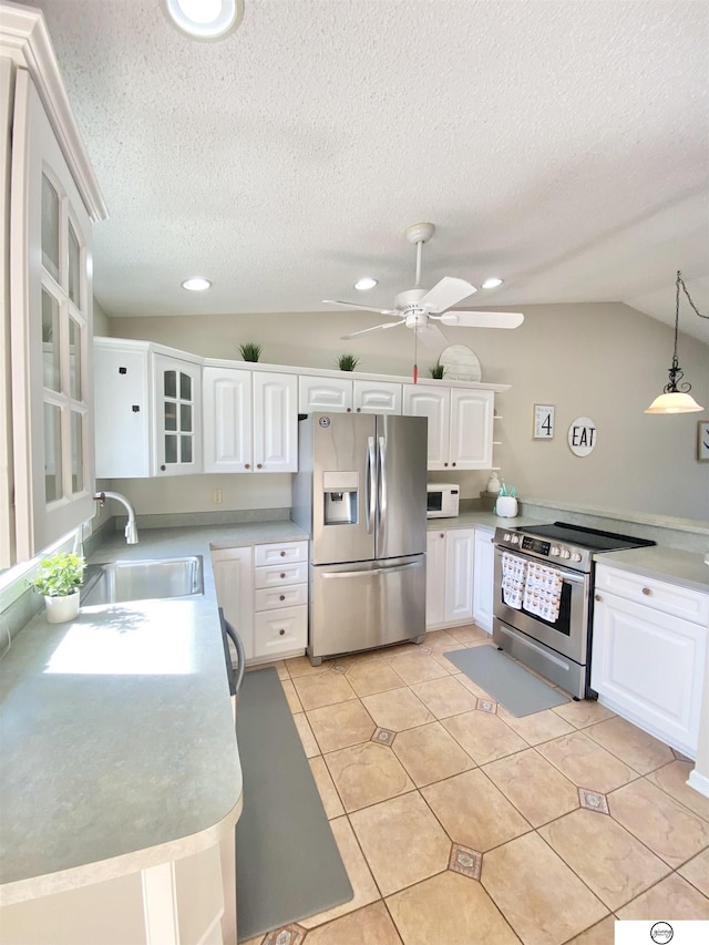 kitchen featuring a ceiling fan, a sink, stainless steel appliances, vaulted ceiling, and white cabinets