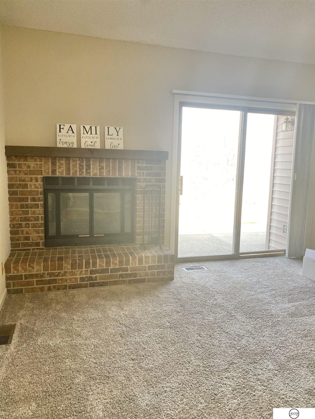 unfurnished living room with visible vents, a textured ceiling, a brick fireplace, and carpet flooring