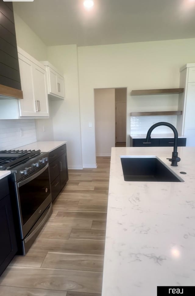 kitchen featuring stainless steel gas stove, a sink, tasteful backsplash, wall chimney exhaust hood, and white cabinets