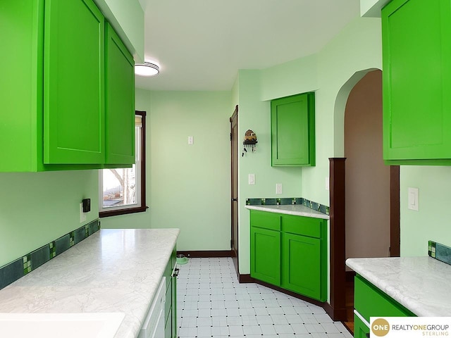 kitchen with light floors, arched walkways, white dishwasher, light countertops, and green cabinets