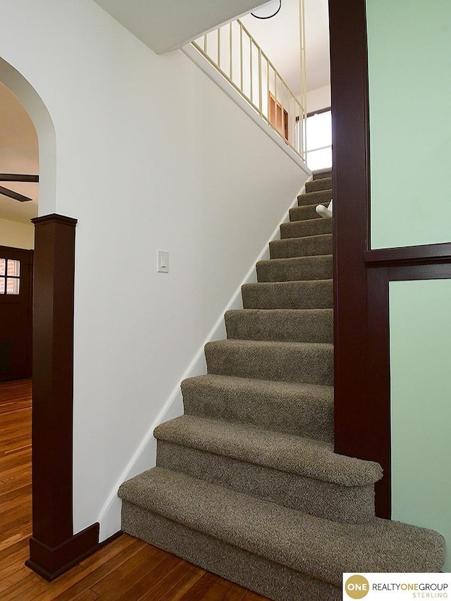 staircase featuring arched walkways, baseboards, a ceiling fan, and wood finished floors