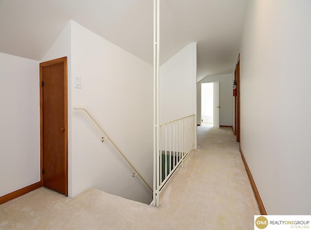 hallway with vaulted ceiling, an upstairs landing, light colored carpet, and baseboards