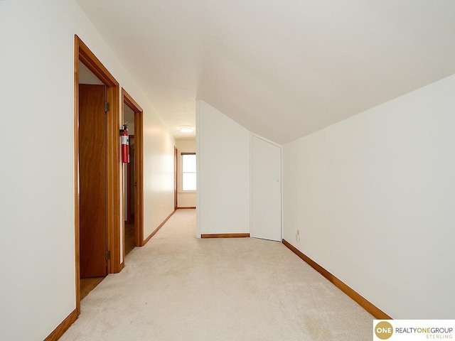 empty room with light colored carpet, baseboards, and vaulted ceiling