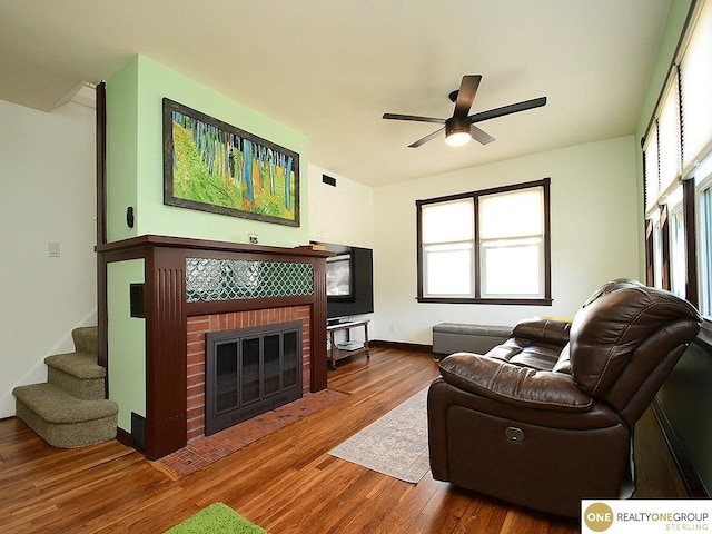 living room with a brick fireplace, baseboards, stairway, wood finished floors, and a ceiling fan