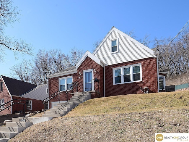 view of front of home with a front lawn, cooling unit, and brick siding