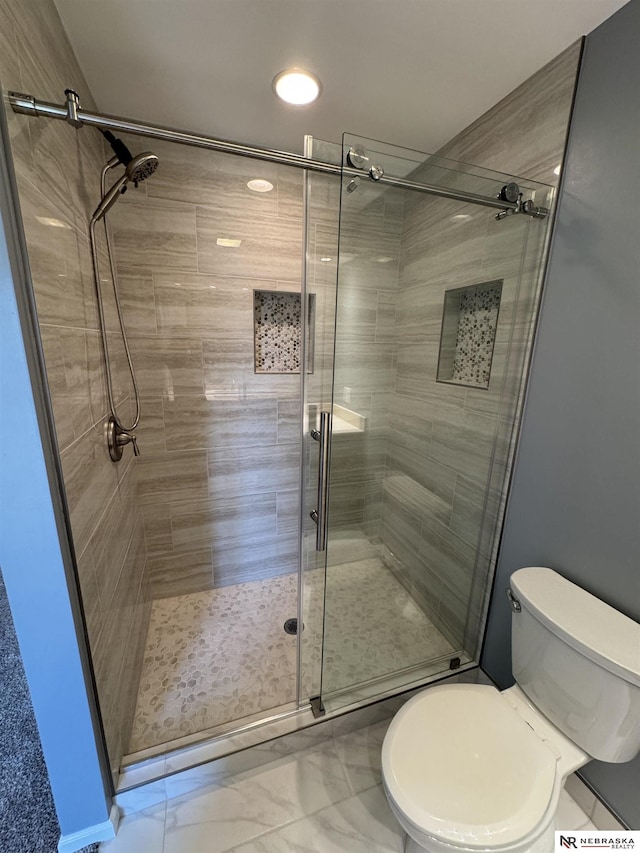 bathroom featuring toilet, marble finish floor, and a shower stall