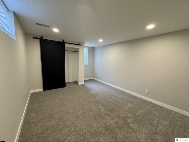 below grade area with visible vents, dark carpet, recessed lighting, a barn door, and baseboards