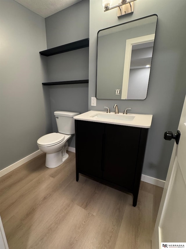 bathroom featuring toilet, a textured ceiling, wood finished floors, baseboards, and vanity