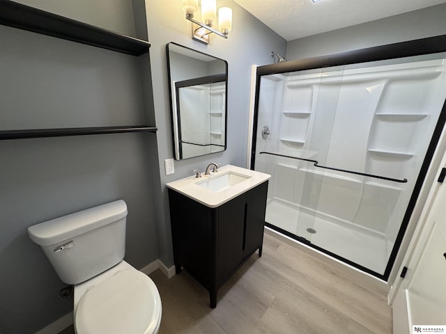 full bathroom featuring vanity, wood finished floors, a shower stall, a textured ceiling, and toilet