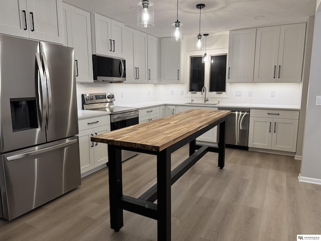 kitchen with backsplash, decorative light fixtures, light wood-style flooring, stainless steel appliances, and a sink