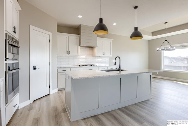 kitchen featuring light wood-style flooring, a sink, white cabinetry, stainless steel appliances, and decorative backsplash