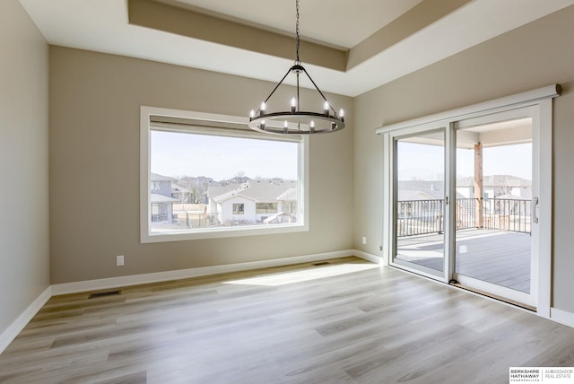 spare room with a healthy amount of sunlight, a raised ceiling, and an inviting chandelier