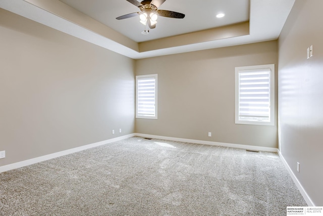 carpeted empty room with a raised ceiling, a ceiling fan, baseboards, and visible vents