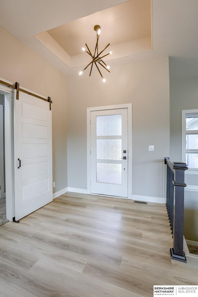 entryway with a notable chandelier, a barn door, baseboards, light wood-style floors, and a raised ceiling