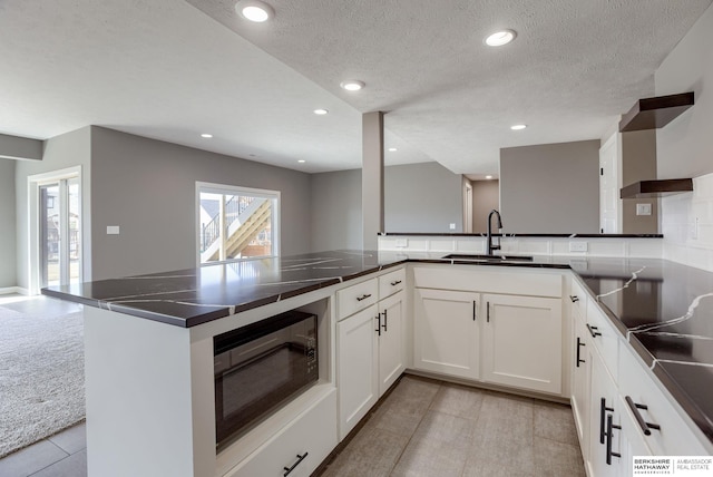 kitchen featuring white cabinetry, dark countertops, recessed lighting, and a sink