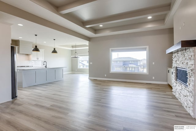 unfurnished living room with light wood-style flooring, a fireplace, a tray ceiling, and a sink