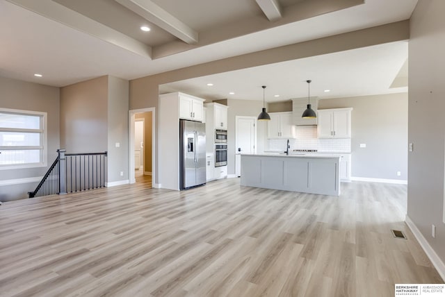 unfurnished living room with beam ceiling, baseboards, light wood-style floors, and a sink