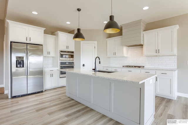 kitchen featuring an island with sink, light wood-type flooring, stainless steel appliances, white cabinetry, and a sink