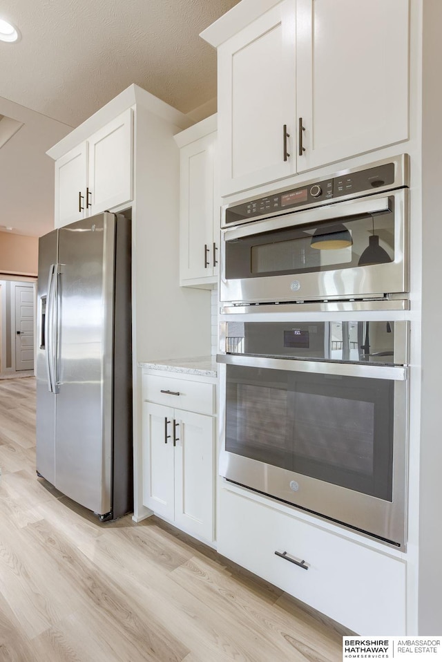 kitchen featuring light wood-type flooring, a textured ceiling, appliances with stainless steel finishes, and white cabinets