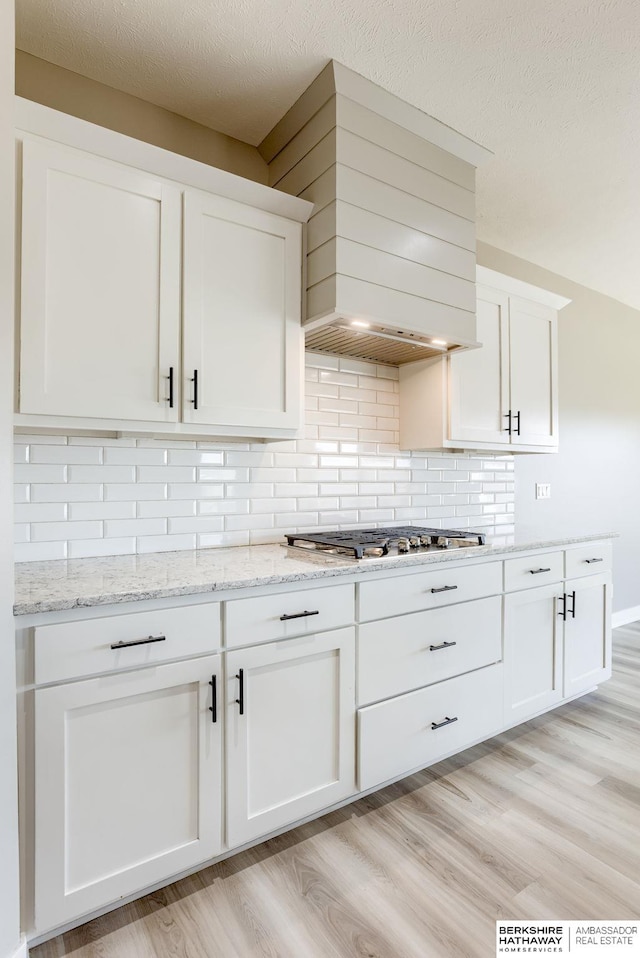 kitchen featuring white cabinetry, stainless steel gas stovetop, light wood-type flooring, and backsplash