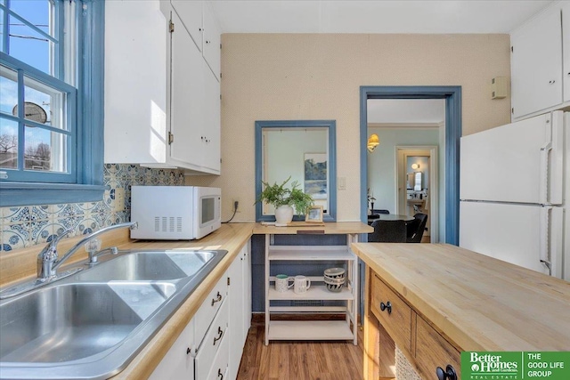 kitchen with a sink, white appliances, wooden counters, and white cabinets