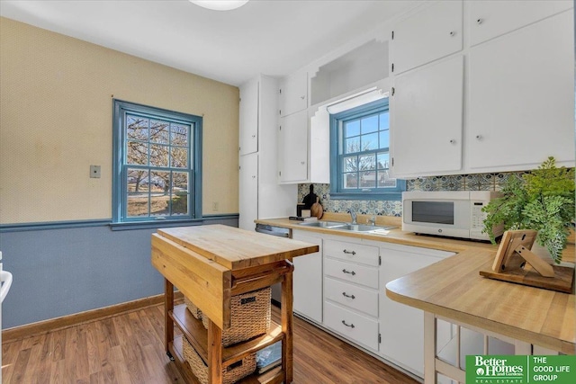 kitchen featuring wood finished floors, white microwave, a sink, light countertops, and white cabinets