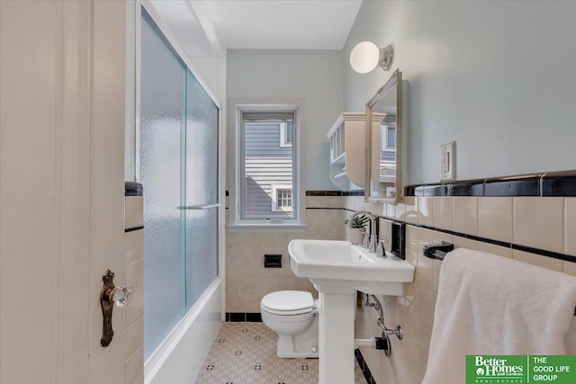 bathroom with a wainscoted wall, toilet, tile patterned floors, tile walls, and a sink