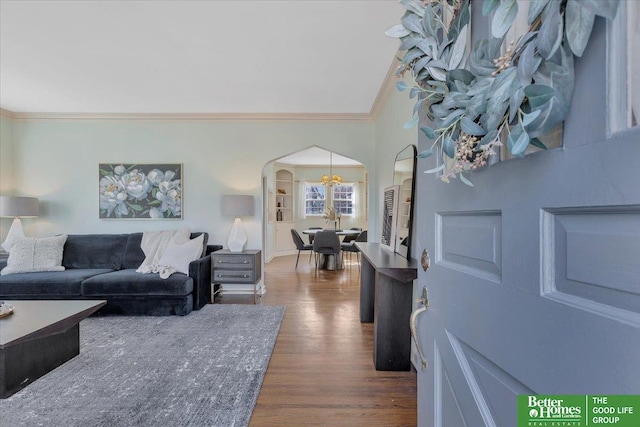 living area with arched walkways, a notable chandelier, ornamental molding, and dark wood-style flooring