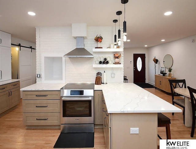 kitchen featuring light wood finished floors, wall chimney range hood, a kitchen bar, stainless steel range with electric cooktop, and a peninsula