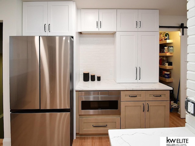 kitchen with light wood-style flooring, backsplash, white cabinetry, freestanding refrigerator, and light stone countertops