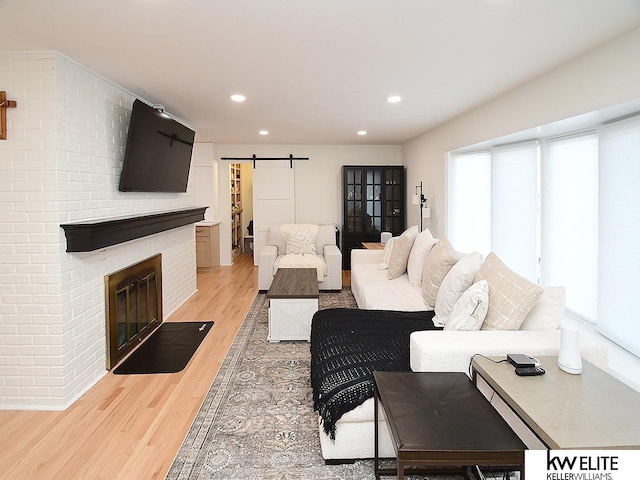 living room featuring recessed lighting, a brick fireplace, light wood-type flooring, and a barn door